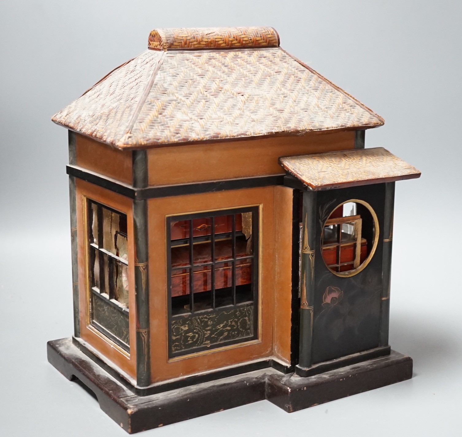 A Japanese lacquer 'house' with pitched wicker roof and opening side and front sections revealing internal shelves and six lacquer boxes and a small glass painted panel, ‘house’ height 28.5 cms high